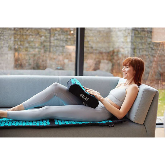 Mergina sėdi ant didelio akupunktūros kilimėlio ir masažuoja delnus su ERGO spygliuota pagalve